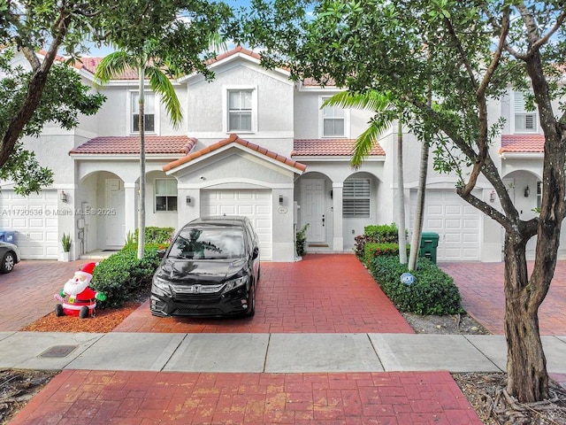 mediterranean / spanish-style home featuring a tile roof, stucco siding, decorative driveway, and an attached garage