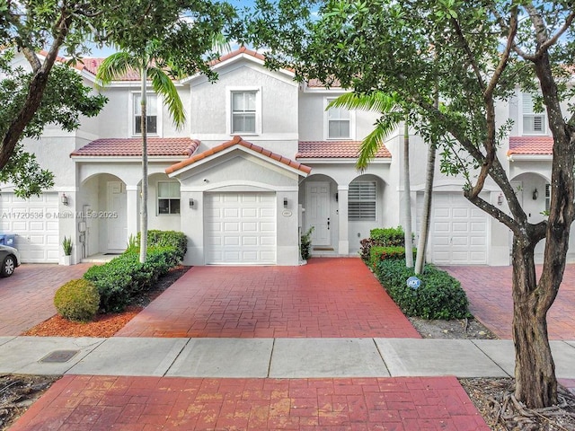 mediterranean / spanish-style home with a tile roof, stucco siding, decorative driveway, and an attached garage
