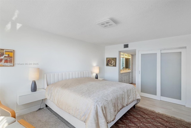 bedroom featuring hardwood / wood-style floors, a textured ceiling, and ensuite bath