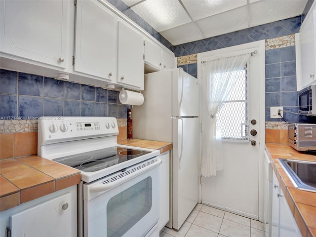 kitchen with sink, a drop ceiling, light tile patterned floors, electric stove, and white cabinets