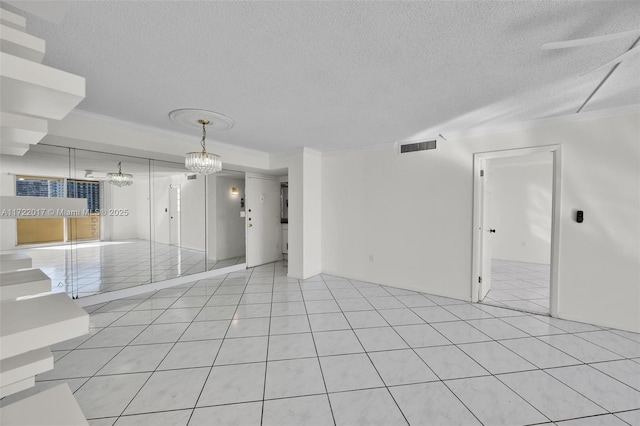 unfurnished room with a textured ceiling, a notable chandelier, ornamental molding, and light tile patterned flooring