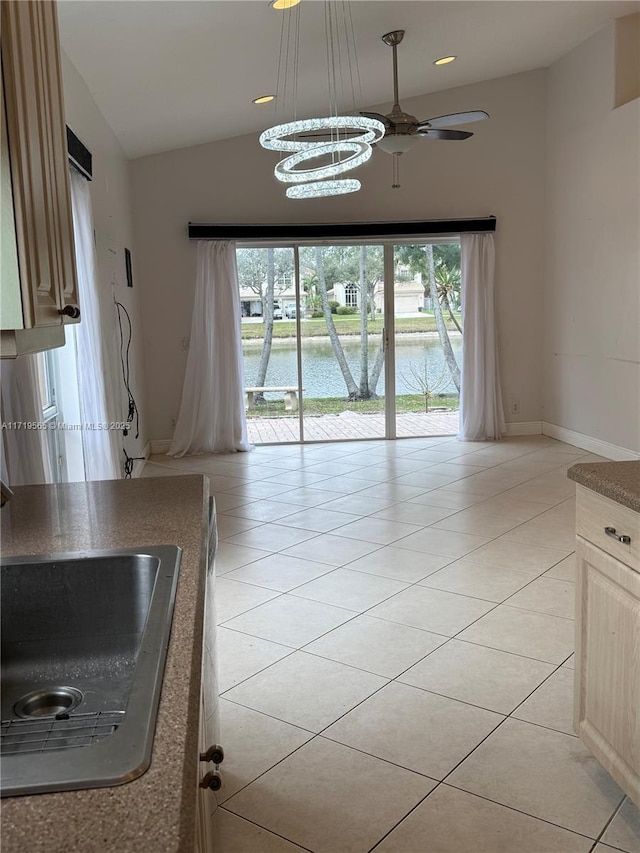 kitchen with sink, ceiling fan with notable chandelier, light tile patterned floors, and a water view