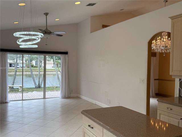 kitchen with ceiling fan with notable chandelier, vaulted ceiling, light tile patterned floors, and a water view