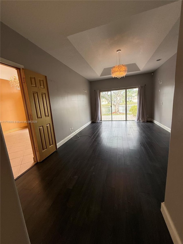 unfurnished room with a raised ceiling, a notable chandelier, and wood-type flooring