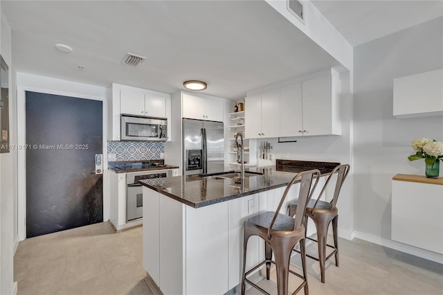 kitchen with kitchen peninsula, appliances with stainless steel finishes, dark stone counters, sink, and white cabinetry