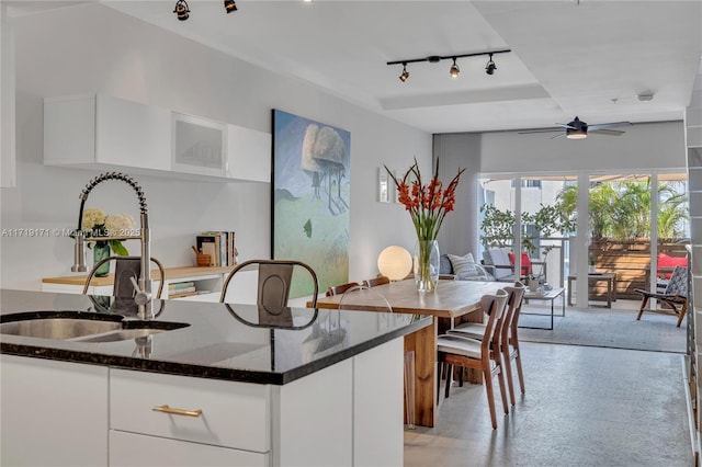 kitchen with dark stone counters, a kitchen island with sink, ceiling fan, sink, and white cabinetry