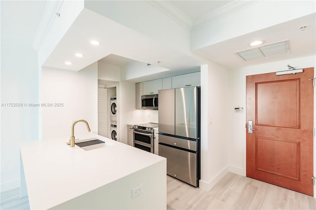 kitchen featuring sink, ornamental molding, stacked washer / drying machine, appliances with stainless steel finishes, and light wood-type flooring