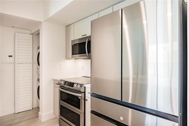 kitchen featuring white cabinetry, stacked washer and dryer, light wood-type flooring, and appliances with stainless steel finishes