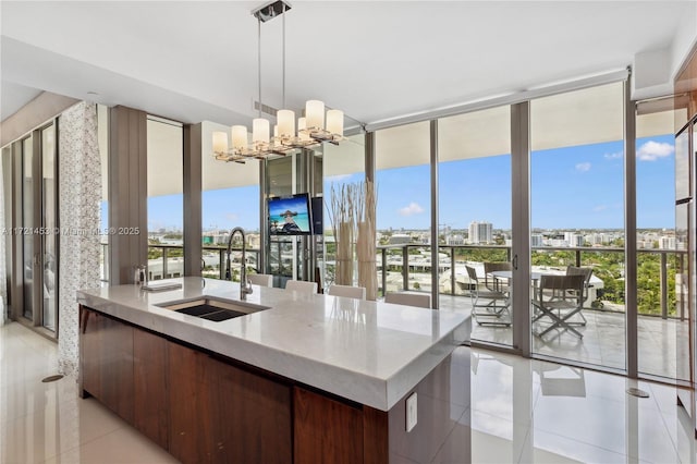 kitchen featuring a wall of windows, light tile patterned floors, sink, pendant lighting, and a center island with sink