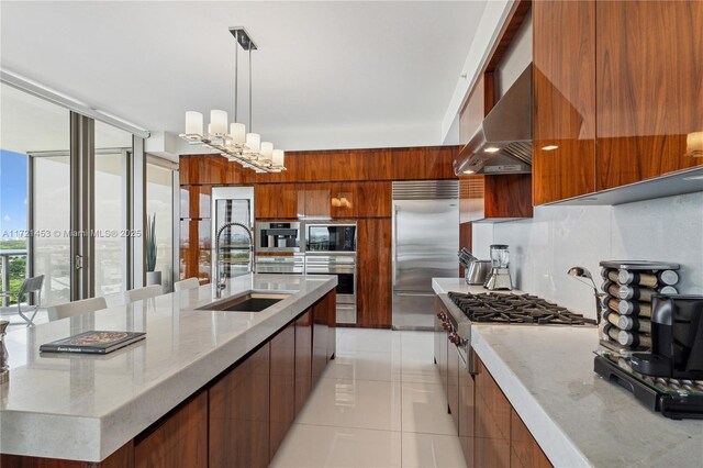 kitchen with pendant lighting, wall chimney exhaust hood, built in appliances, sink, and light tile patterned flooring