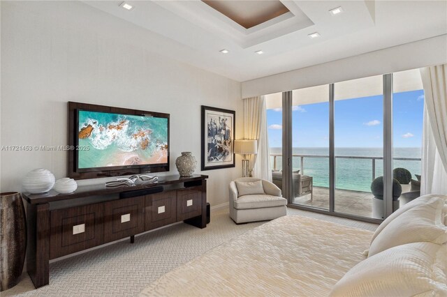 bedroom with a wall of windows, light carpet, a water view, access to outside, and a tray ceiling