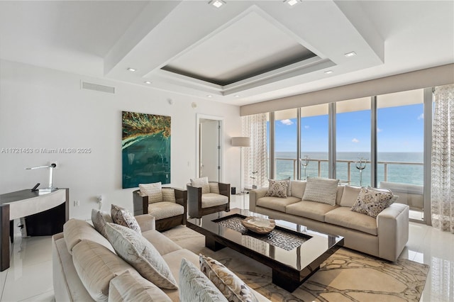 tiled living room with plenty of natural light, a water view, and a tray ceiling