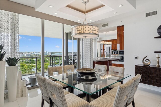 dining area with light tile patterned flooring, floor to ceiling windows, and a raised ceiling