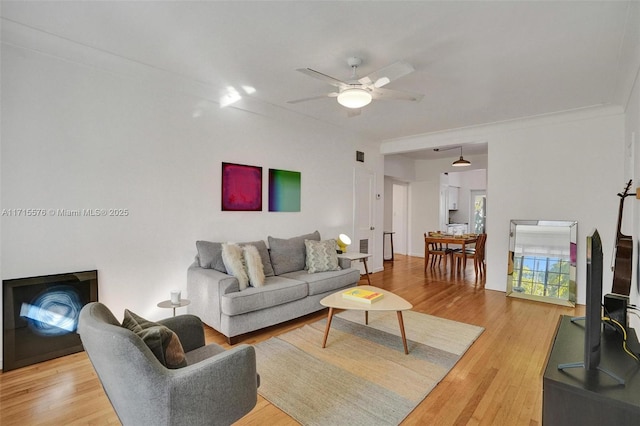 living room featuring ceiling fan, wood-type flooring, and crown molding