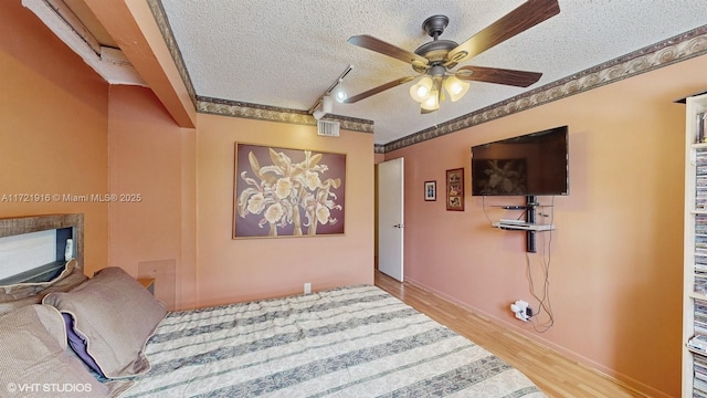 bedroom featuring ceiling fan, rail lighting, light hardwood / wood-style floors, and a textured ceiling