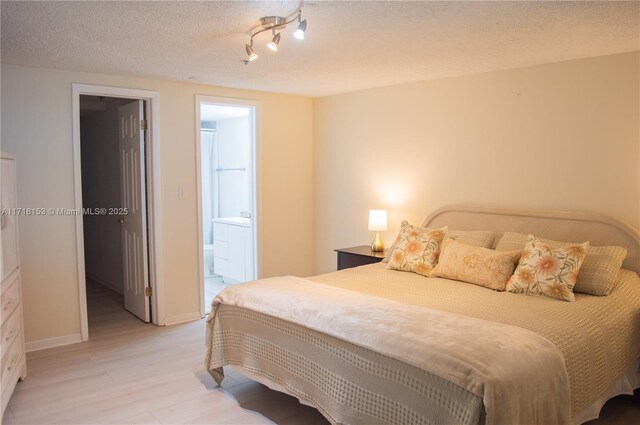 bedroom featuring a textured ceiling, light hardwood / wood-style floors, and ensuite bath