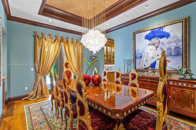 dining space featuring crown molding, a raised ceiling, an inviting chandelier, and light wood-type flooring