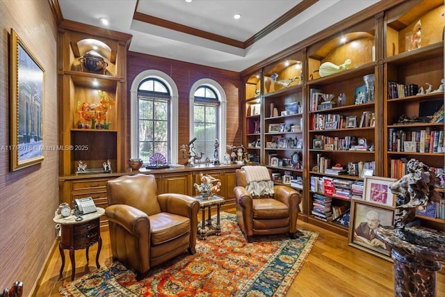 living area with a raised ceiling, crown molding, and light hardwood / wood-style floors