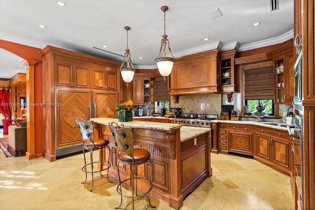 kitchen with pendant lighting, premium range hood, a center island, light stone countertops, and ornate columns