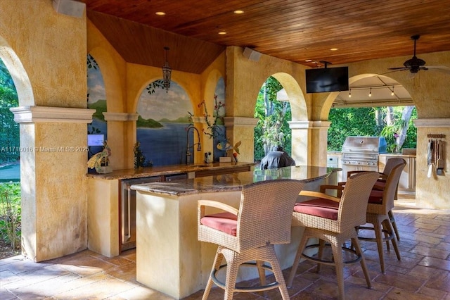 view of patio with ceiling fan, a grill, an outdoor wet bar, and exterior kitchen