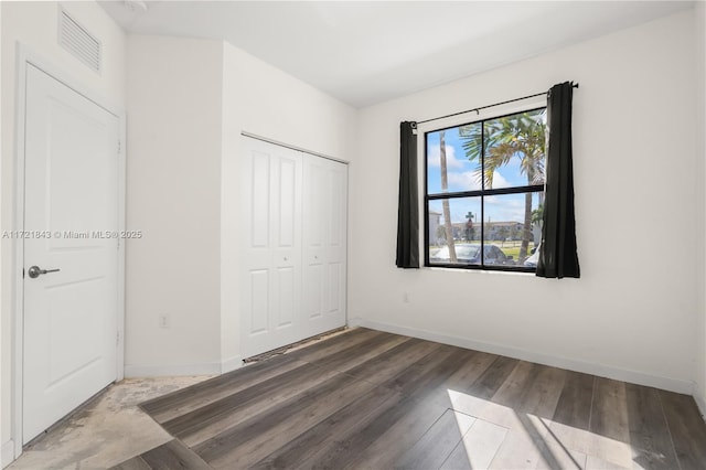 unfurnished bedroom featuring dark hardwood / wood-style flooring, a closet, and multiple windows