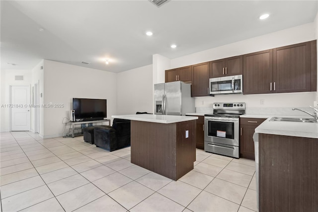 kitchen with sink, light tile patterned floors, a kitchen island, dark brown cabinetry, and stainless steel appliances