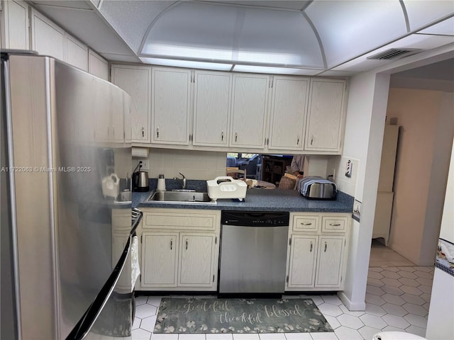 kitchen with sink, tasteful backsplash, cream cabinets, light tile patterned floors, and appliances with stainless steel finishes