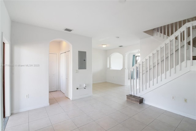 empty room featuring arched walkways, visible vents, baseboards, stairway, and electric panel