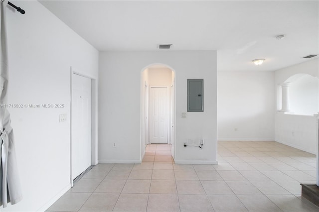 empty room with visible vents, light tile patterned floors, arched walkways, and electric panel