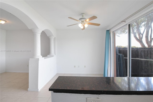 kitchen featuring arched walkways, baseboards, ceiling fan, tile patterned flooring, and ornate columns