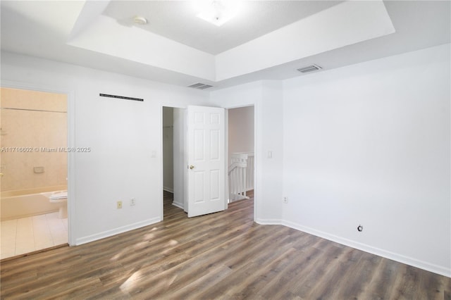 unfurnished bedroom with a raised ceiling, ensuite bath, and dark hardwood / wood-style floors