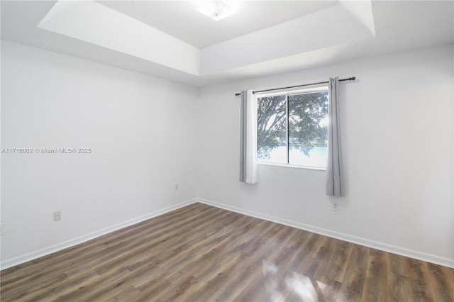 unfurnished room with baseboards, a raised ceiling, and dark wood finished floors