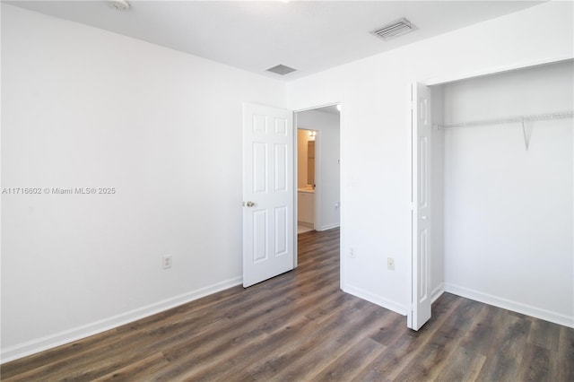 unfurnished bedroom featuring dark wood-type flooring, a closet, visible vents, and baseboards