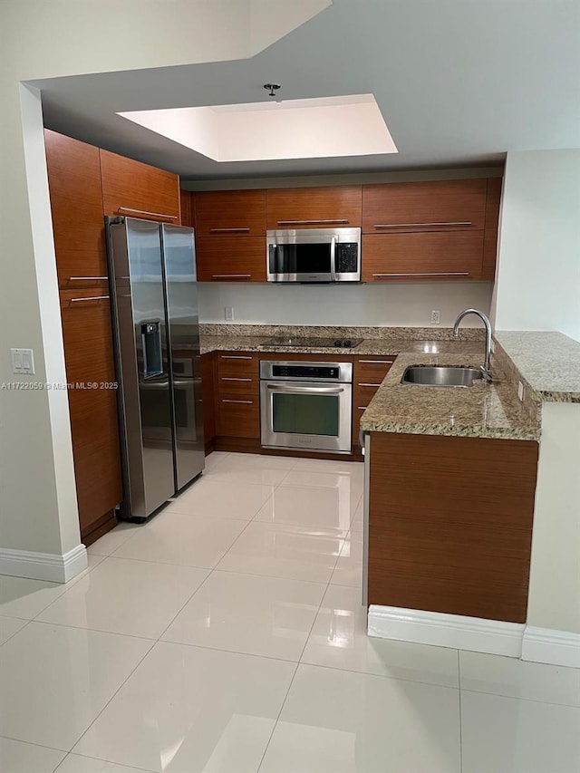 kitchen with light stone countertops, appliances with stainless steel finishes, kitchen peninsula, sink, and light tile patterned floors