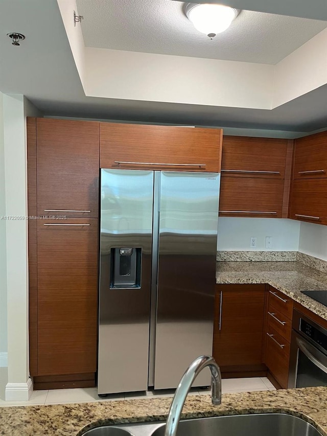 kitchen featuring sink, light stone counters, a textured ceiling, light tile patterned flooring, and appliances with stainless steel finishes