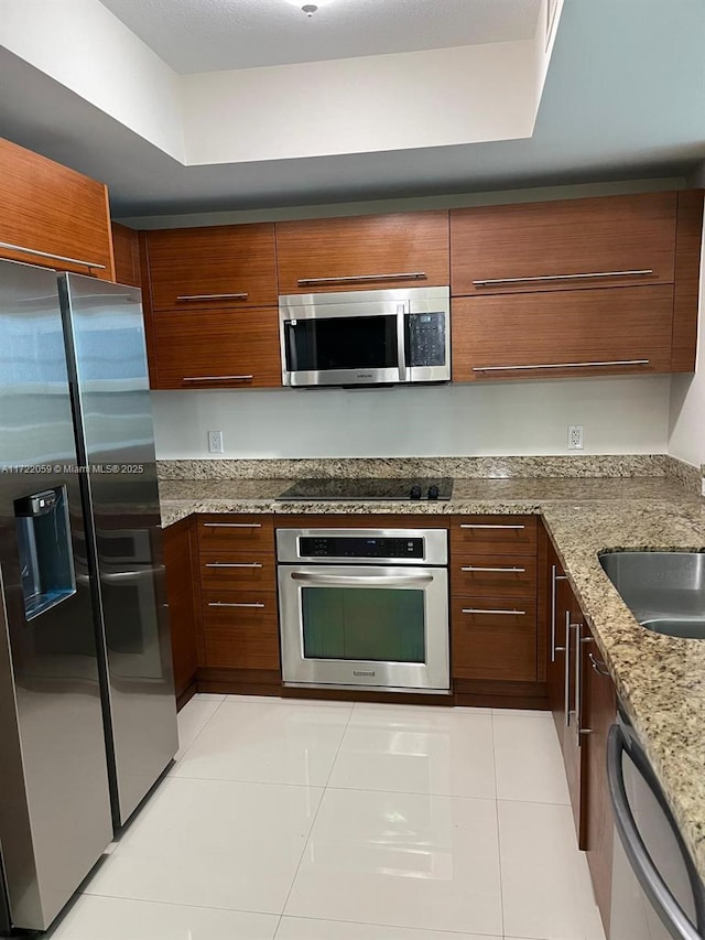 kitchen featuring appliances with stainless steel finishes, light stone counters, a raised ceiling, sink, and light tile patterned floors