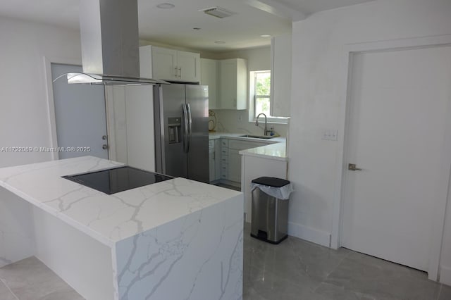 kitchen with light stone counters, island range hood, sink, stainless steel fridge with ice dispenser, and white cabinetry