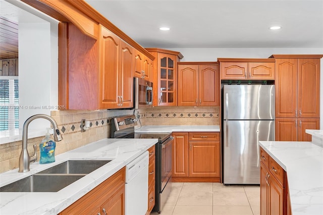 kitchen with sink, light tile patterned floors, stainless steel appliances, tasteful backsplash, and light stone countertops