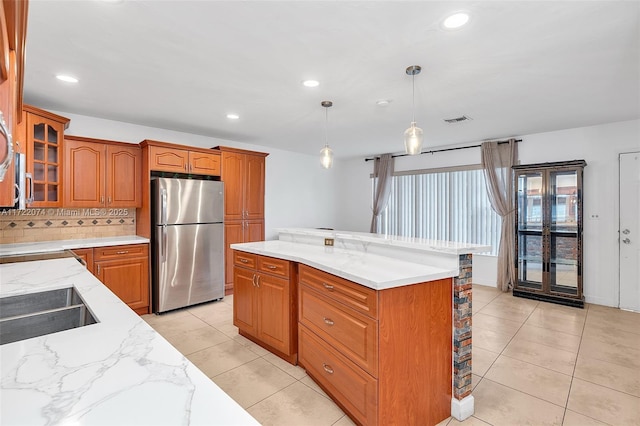 kitchen with pendant lighting, light tile patterned floors, stainless steel fridge, a kitchen island, and decorative backsplash