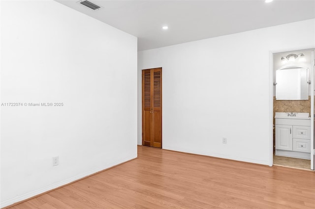 unfurnished bedroom featuring sink, ensuite bath, and light wood-type flooring