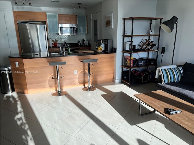 interior space with sink, tasteful backsplash, a breakfast bar area, light tile patterned floors, and appliances with stainless steel finishes