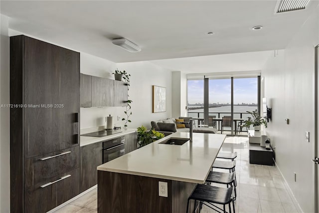 kitchen with sink, a kitchen breakfast bar, an island with sink, oven, and black electric cooktop