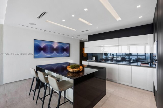 kitchen with a breakfast bar, a kitchen island, decorative backsplash, and white cabinetry