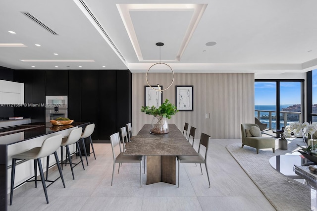 dining room featuring visible vents, a raised ceiling, a water view, and wooden walls