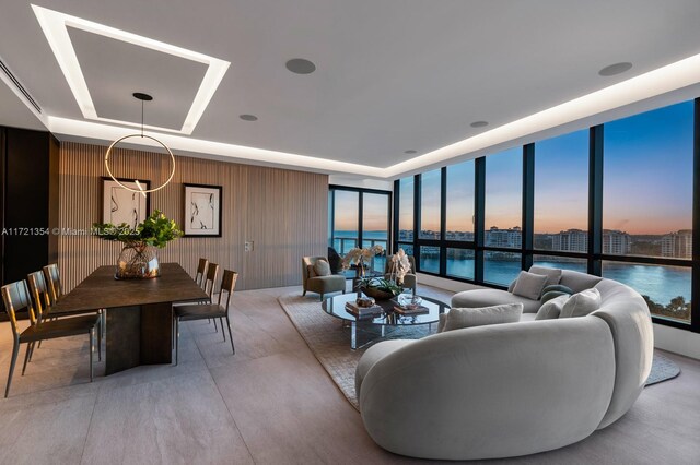 living room featuring a raised ceiling, floor to ceiling windows, and a water view