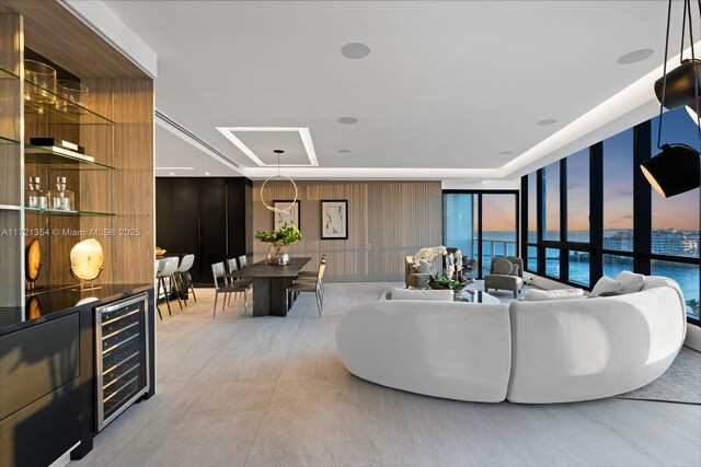 living room with expansive windows, a water view, beverage cooler, and wood walls