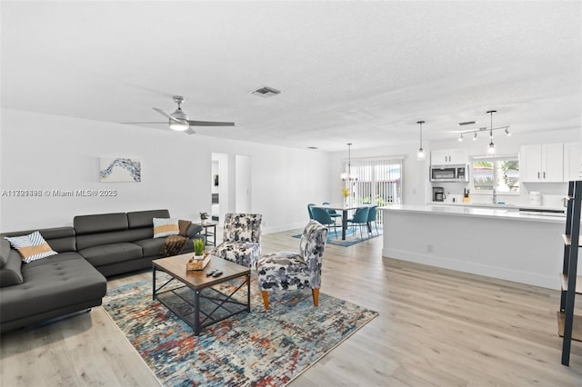 living room with a textured ceiling, light wood-type flooring, ceiling fan, and sink