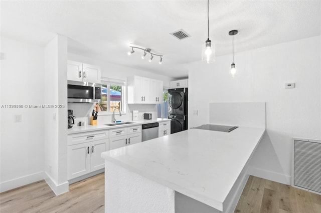 kitchen with white cabinets, pendant lighting, stacked washer / dryer, and black appliances