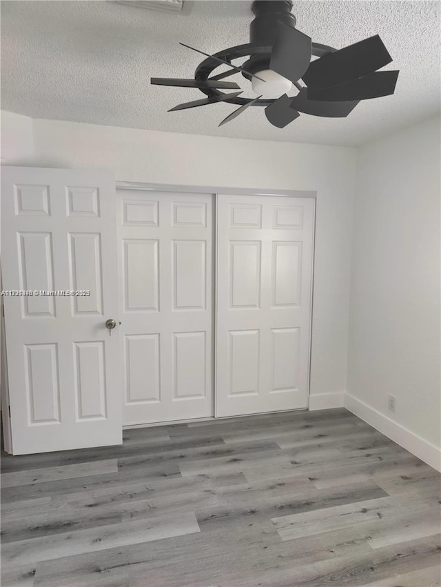 unfurnished bedroom with a textured ceiling, hardwood / wood-style flooring, a closet, and ceiling fan