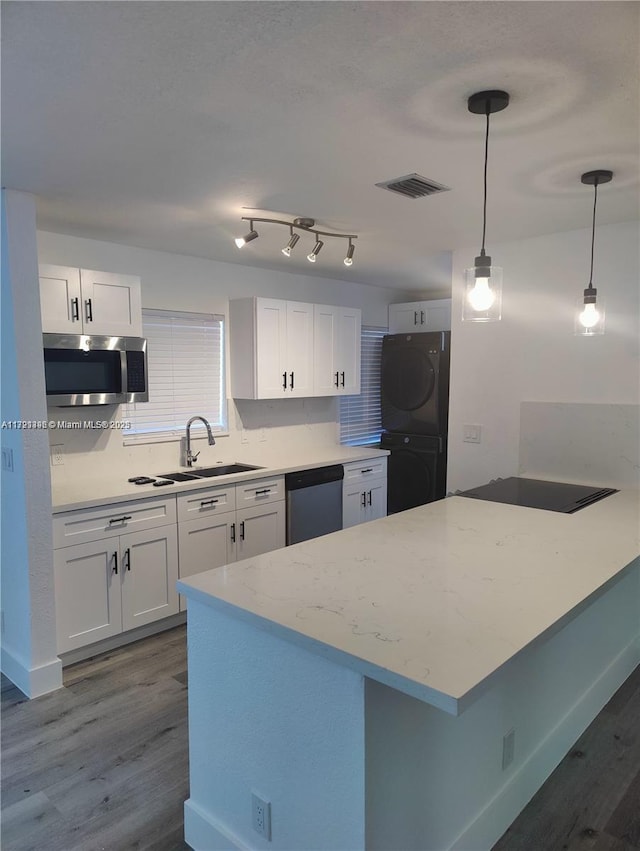 kitchen with appliances with stainless steel finishes, stacked washer and clothes dryer, white cabinets, dark hardwood / wood-style floors, and hanging light fixtures